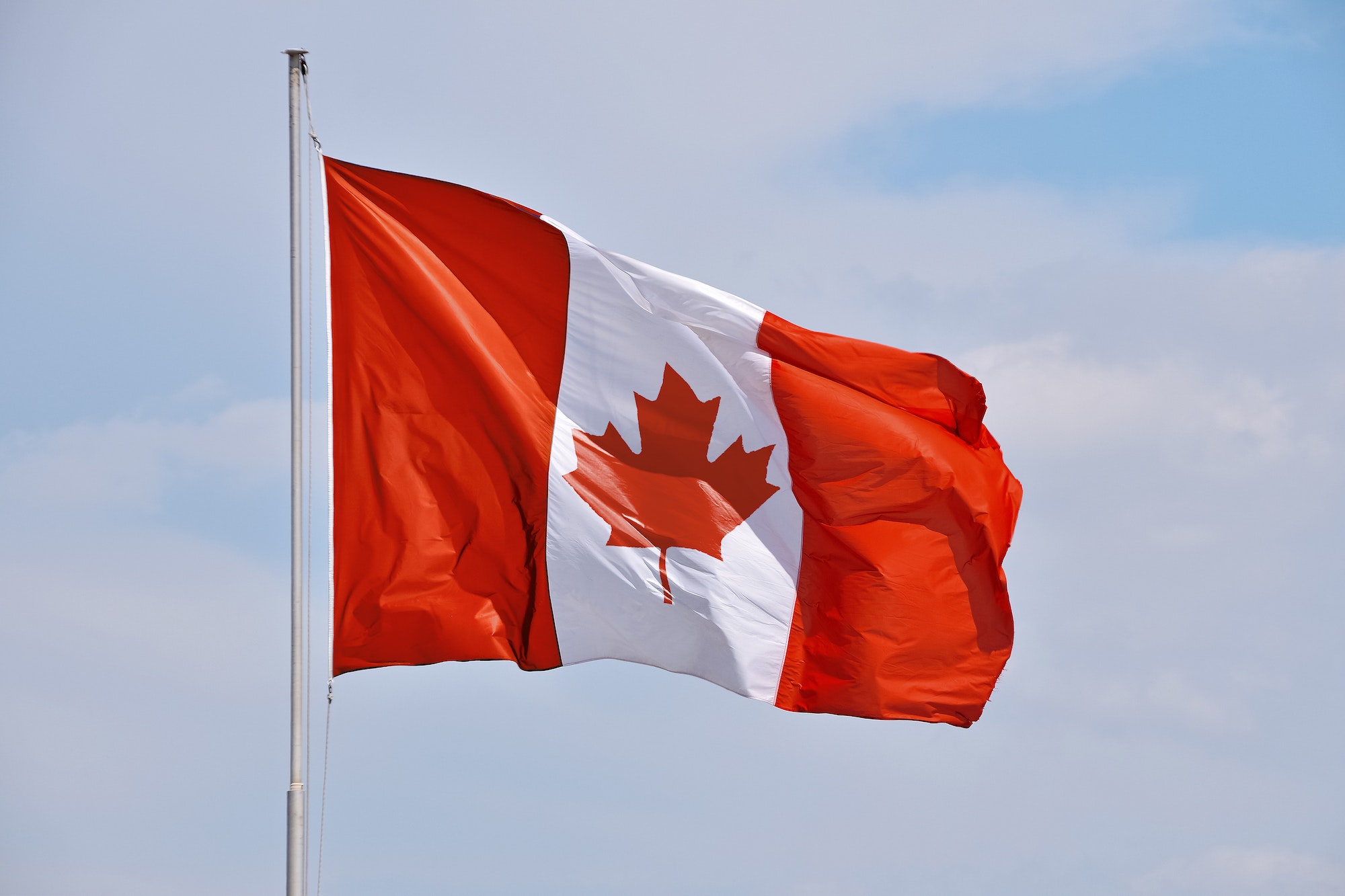 Canadian flag waving in cloudy blue sky